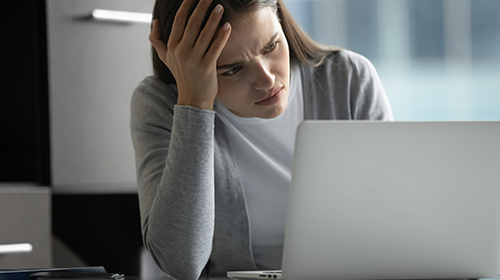 Junge Frau guckt verärgert auf ihren Laptop, weil sie nachpassenden Unternehmensinformationen sucht
