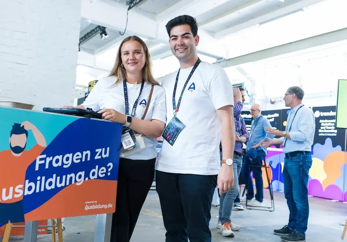 Zwei Mitarbeiter:innen von Ausbildung.de lächeln in die Kamera